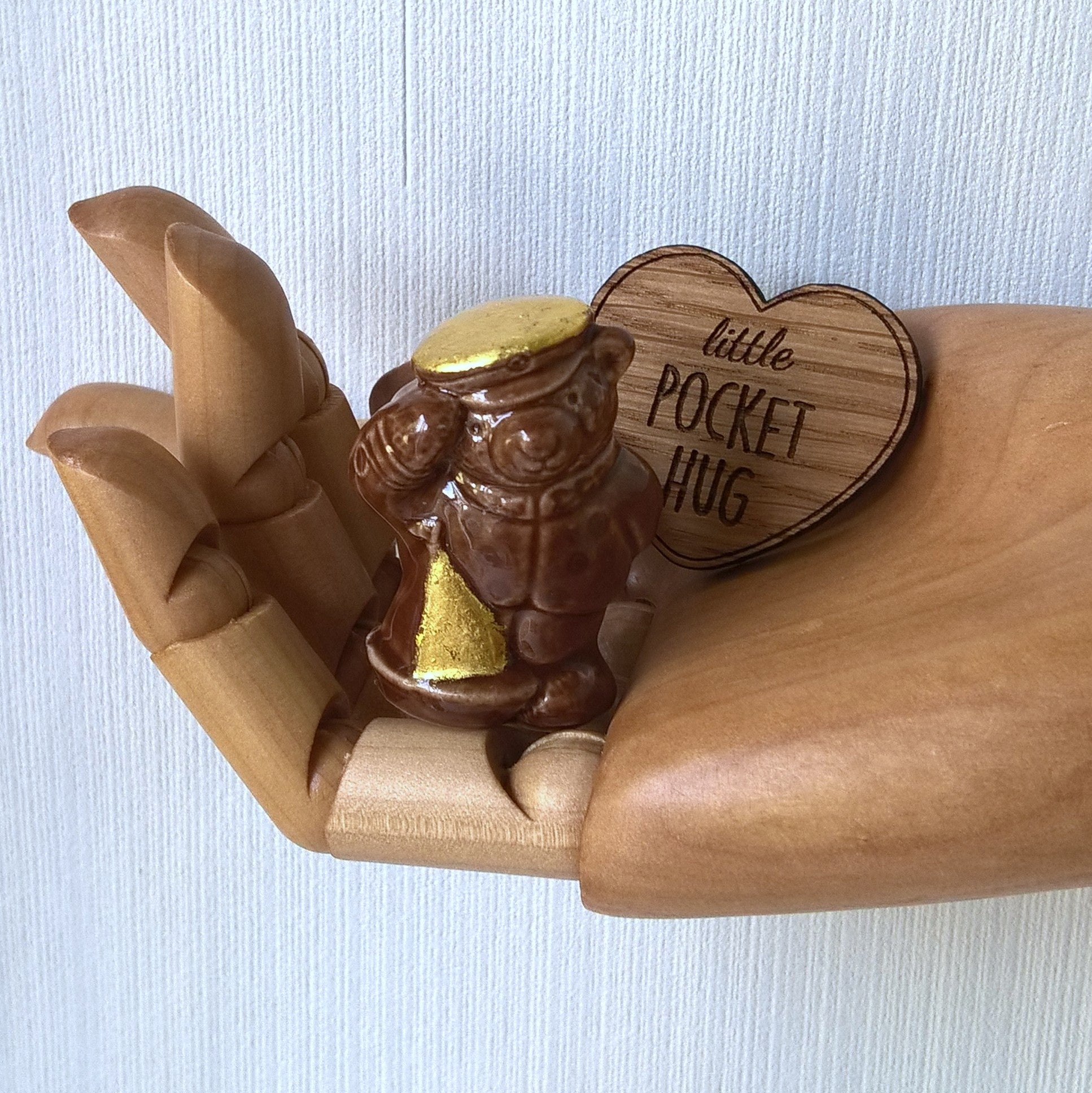 Miniature brown ceramic sailor bear fits into the palm of a hand, along with the wooden heart pocket hug 