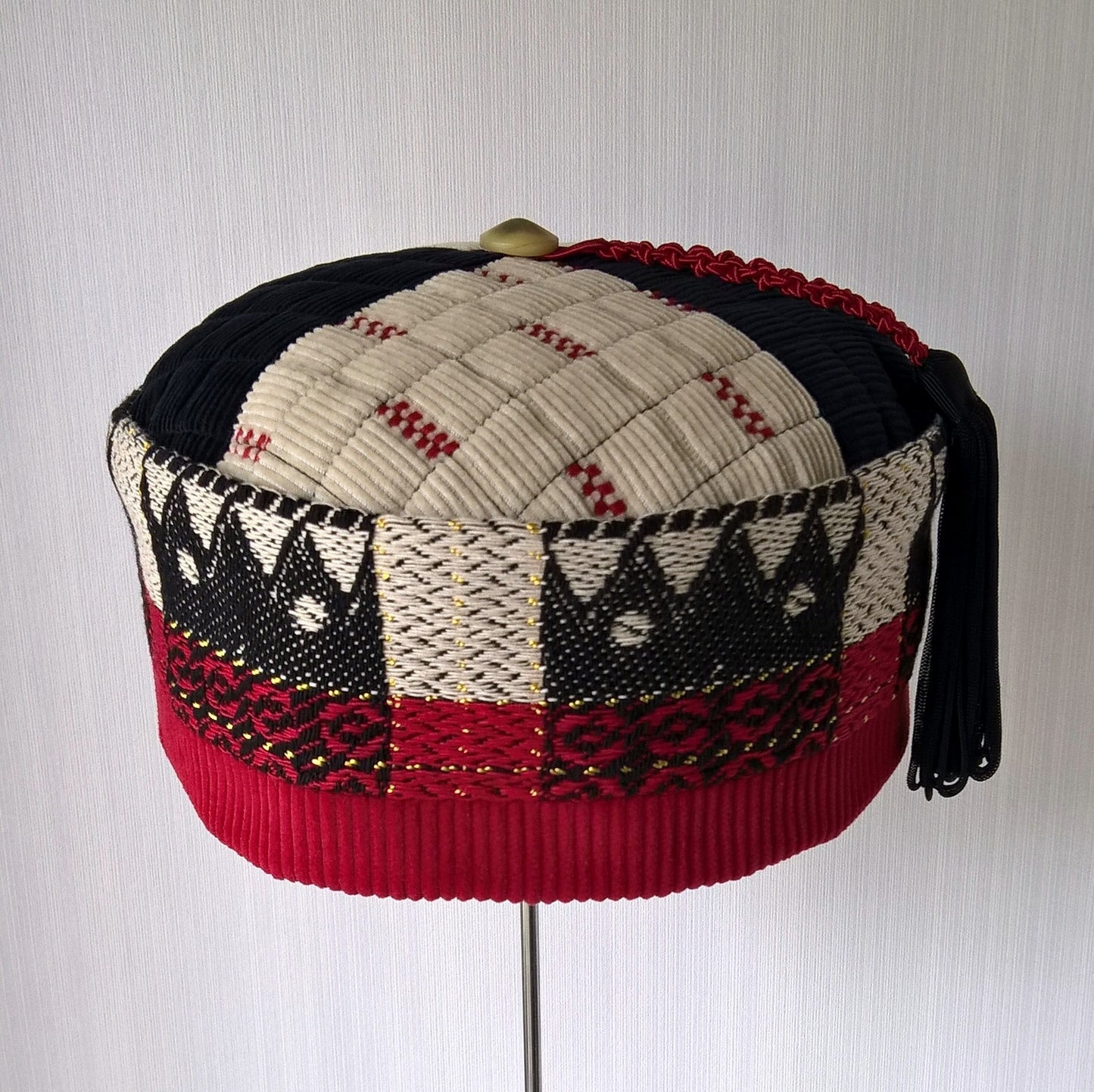 Front view of black, red and cream ethnic patterned smoking cap with tassel