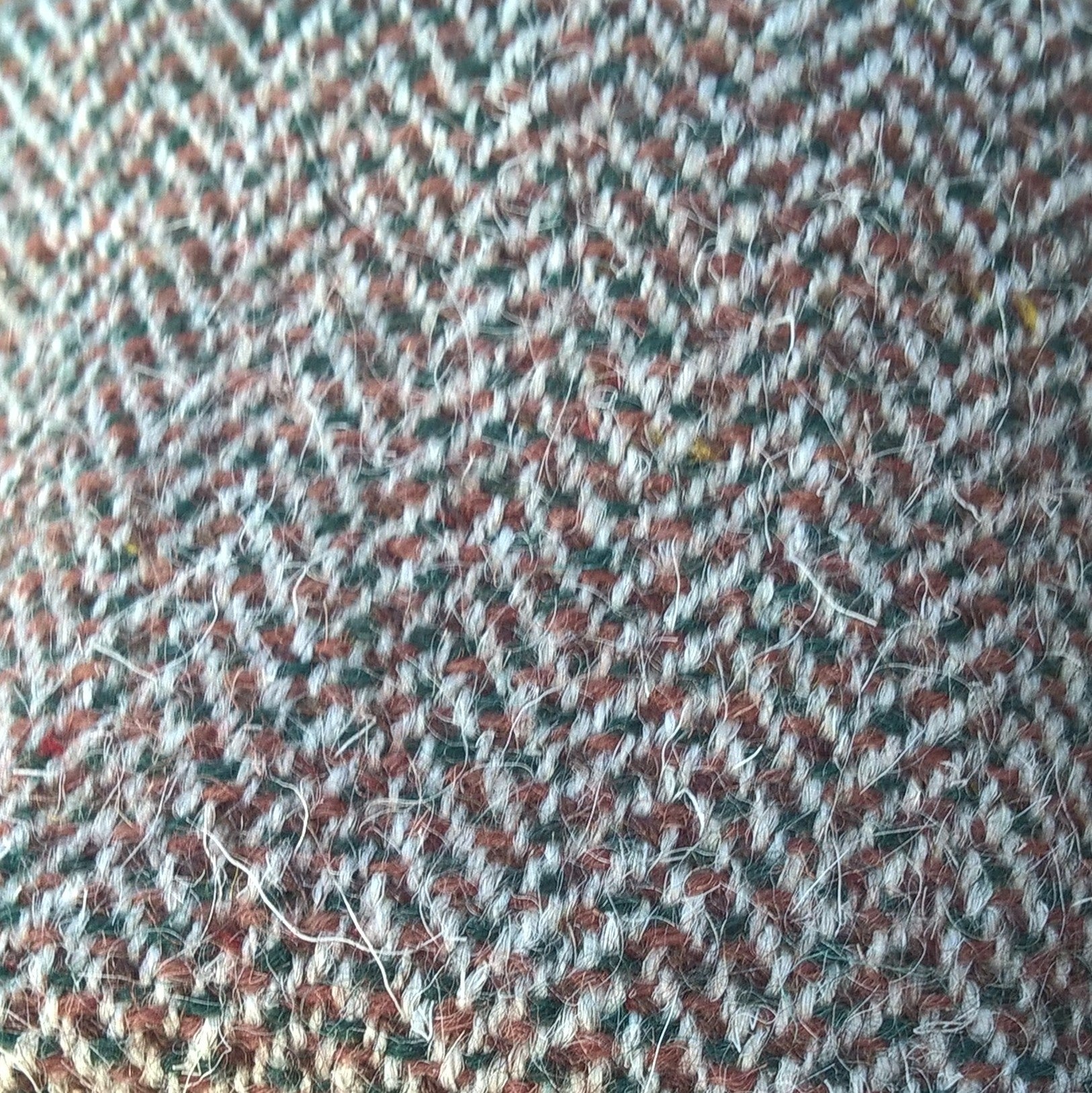 Close up of Harris Tweed herringbone fabric in brown, off white and dark green 