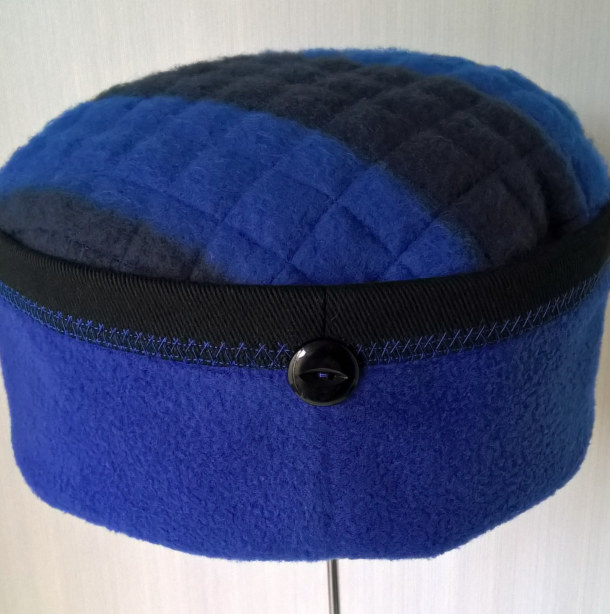 Cobalt blue fleece hat with black button detail at centre back