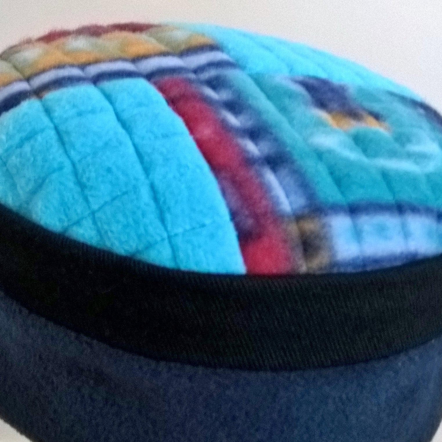 The turquoise and multi coloured patchwork tip of the brimless fleece cap