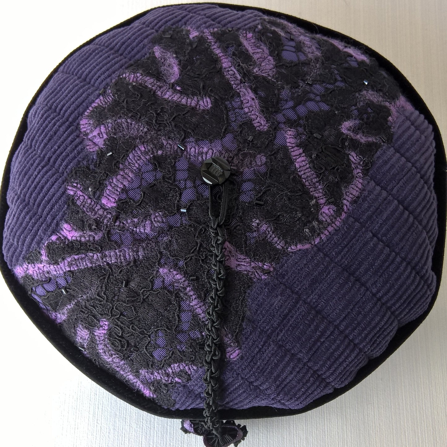 A combination of needle and wet felting is used to combine lace and wool tops on the tip of the smoking cap, and finished with beading