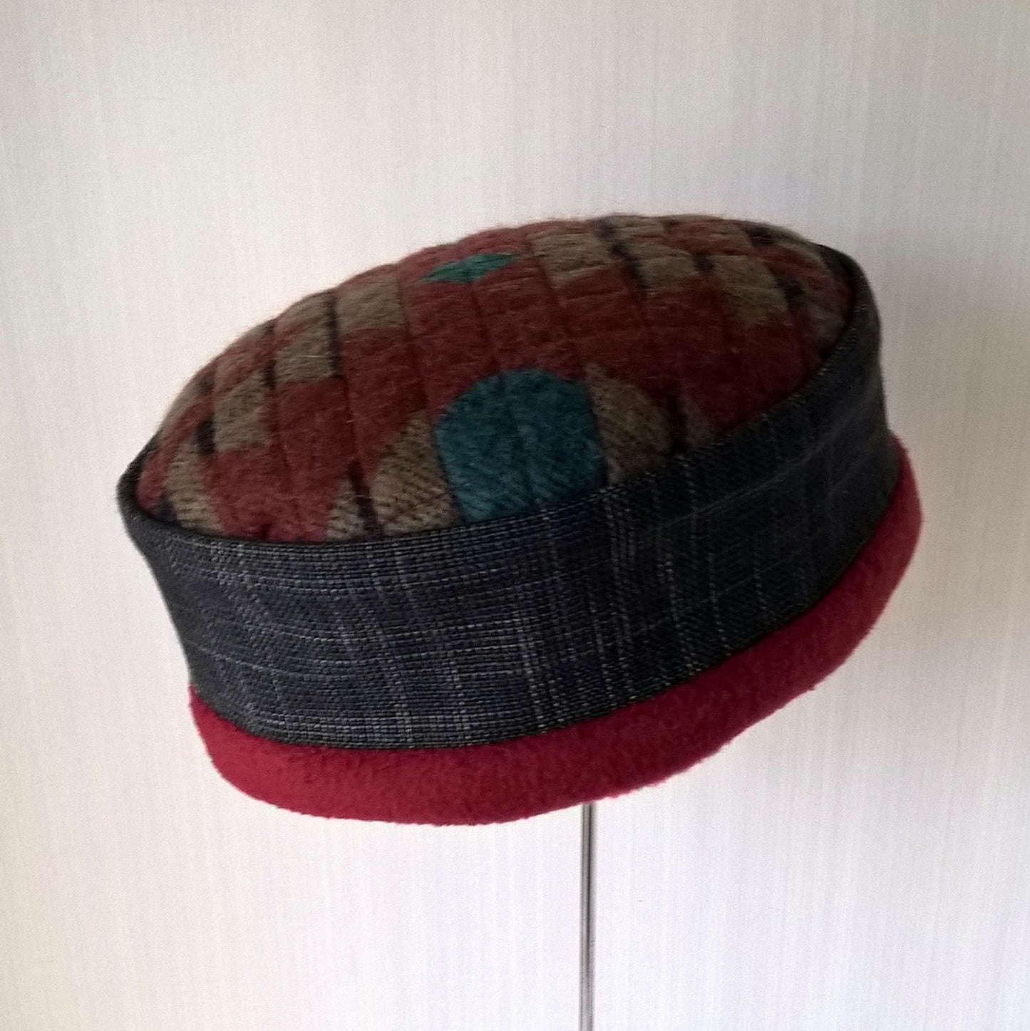 Pillbox shaped hat with Aztec patterned tip, grey hatch crown and raspberry red fleece edging